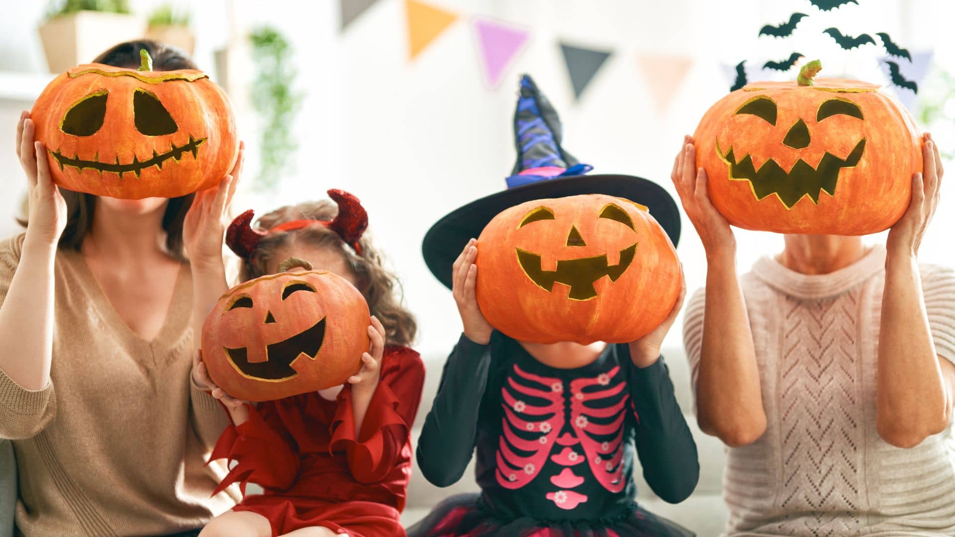 Young family in halloween costumes holding up jack-o-lanterns in front of their faces