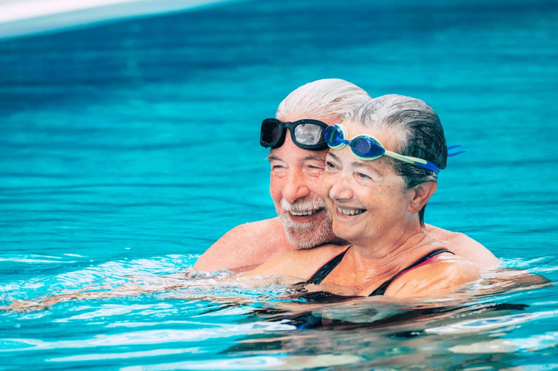 Senior couple in pool wearing goggles smiling