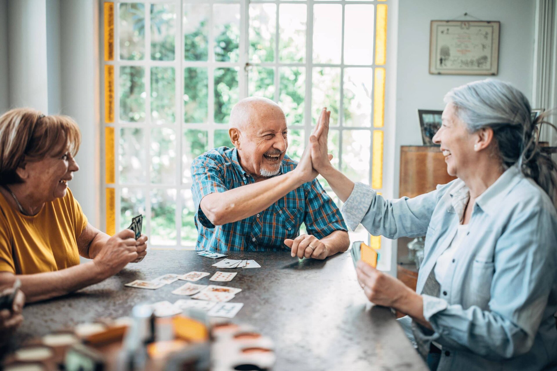 Senior friends highfive at table while they play cards