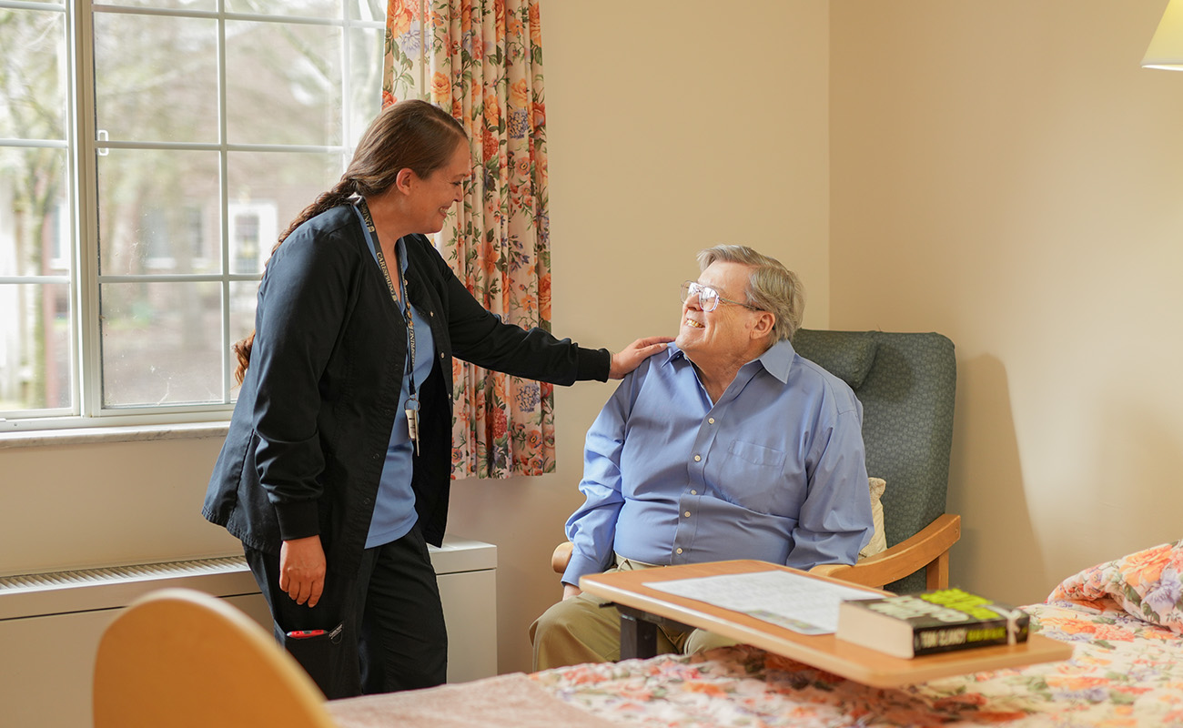 Caregiver interacting with a smiling man in a senior living unit.