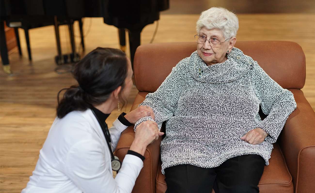 Healthcare worker comforting elderly woman in a senior living unit lounge.