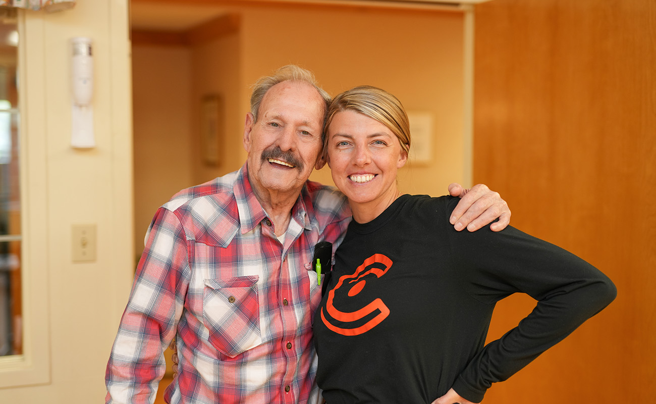 Senior resident and staff member smiling warmly in a community hallway.