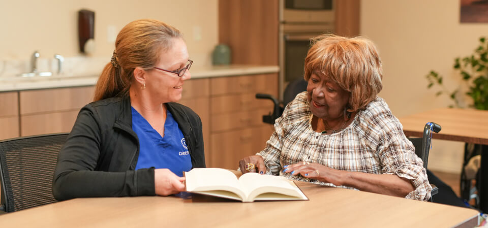 Carespring employee assisting senior woman as she looks through a large book