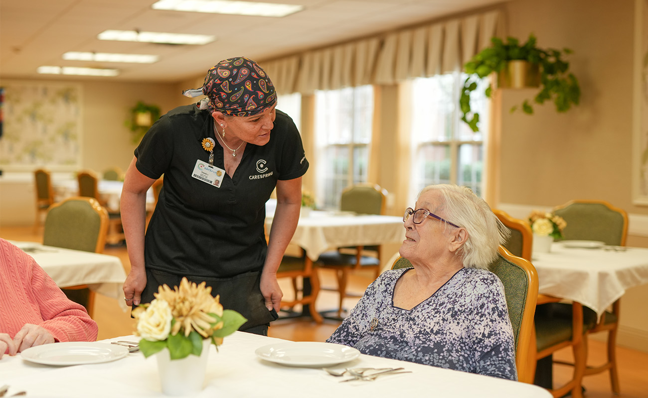 Staff member interacting with resident in a senior living dining area.