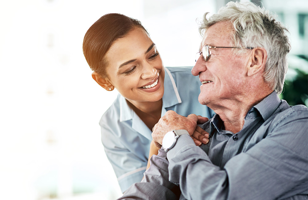 Caregiver smiling at elderly man in community living unit.