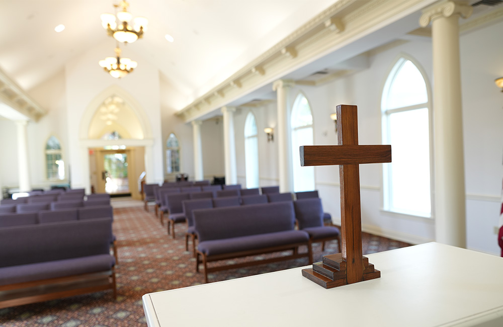 Interior view of a chapel with wooden cross and rows of pews.