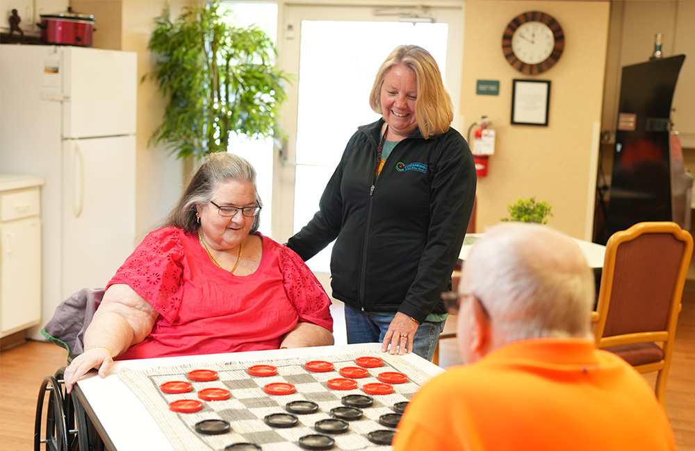 Residents enjoying a game of checkers in the community room with a staff member.