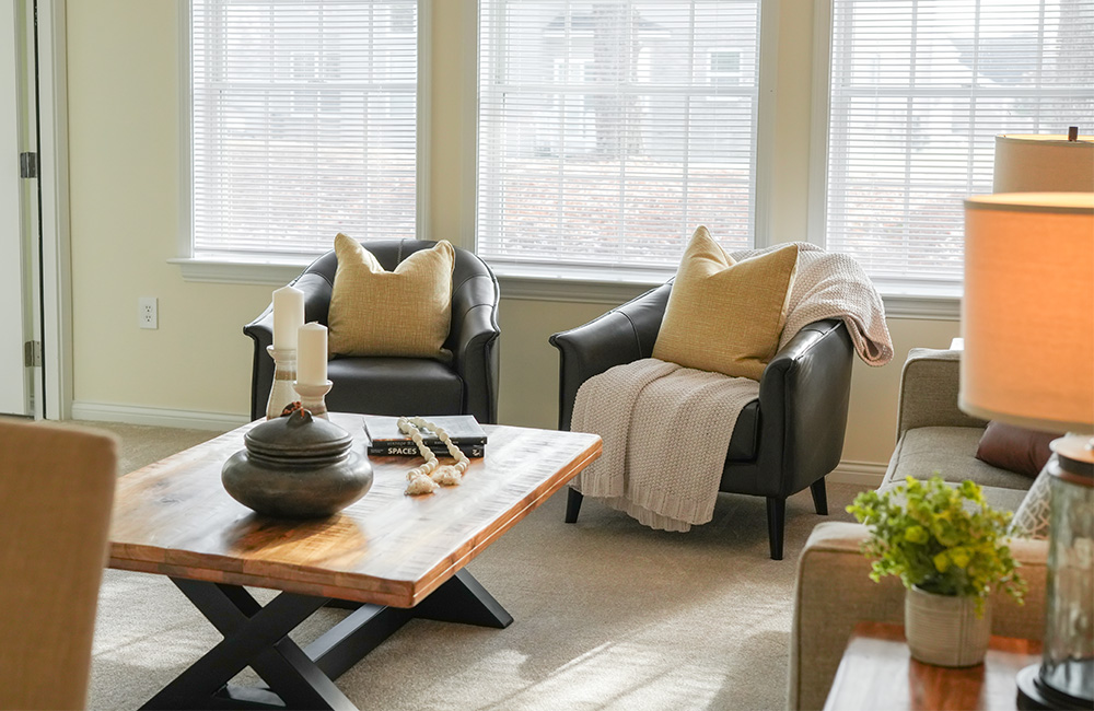 Sunlit living room in senior community unit with cozy chairs and wooden table.