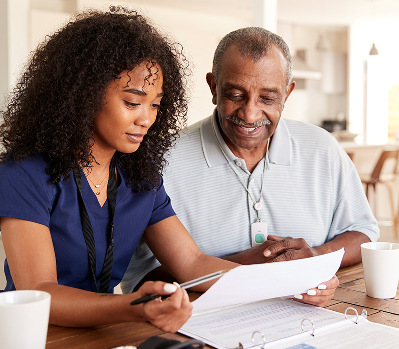 Staff member and senior reviewing documents at a table in a living space.