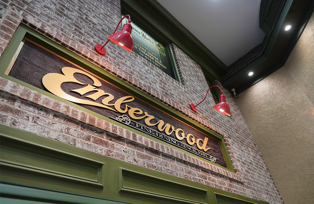 Red brick wall with Emberwood fine dining sign under red lamps.