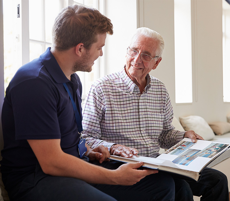 Older man and caregiver discussing photo album in a cozy living space.