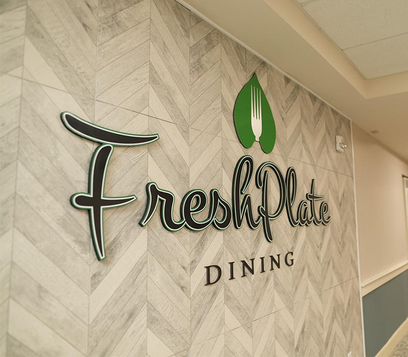 FreshPlate Dining sign on herringbone wall in a senior living community.