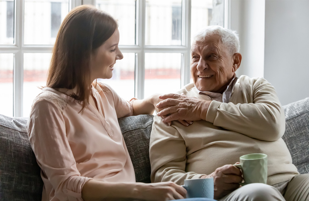 Young woman and elderly man sharing a friendly conversation with mugs.