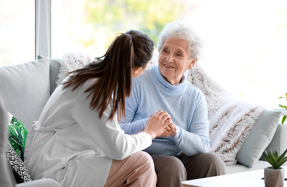 Caregiver engages warmly with a senior woman on a comfortable sofa in bright surroundings.