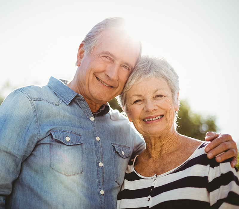 Smiling senior couple embracing in sunny outdoor setting.