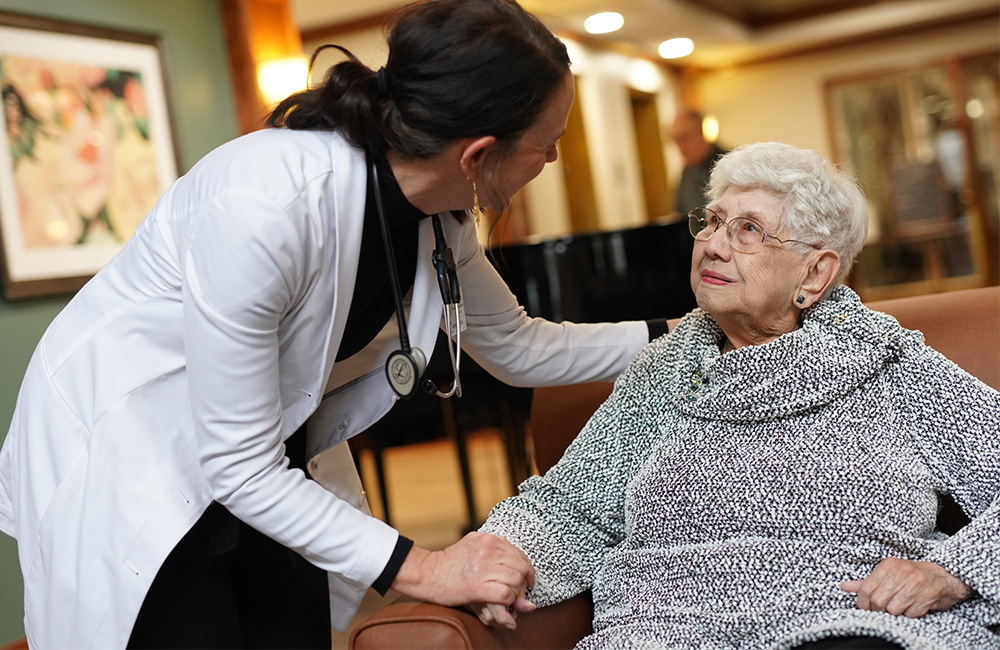 Doctor interacting with a senior resident in a cozy living room setting.