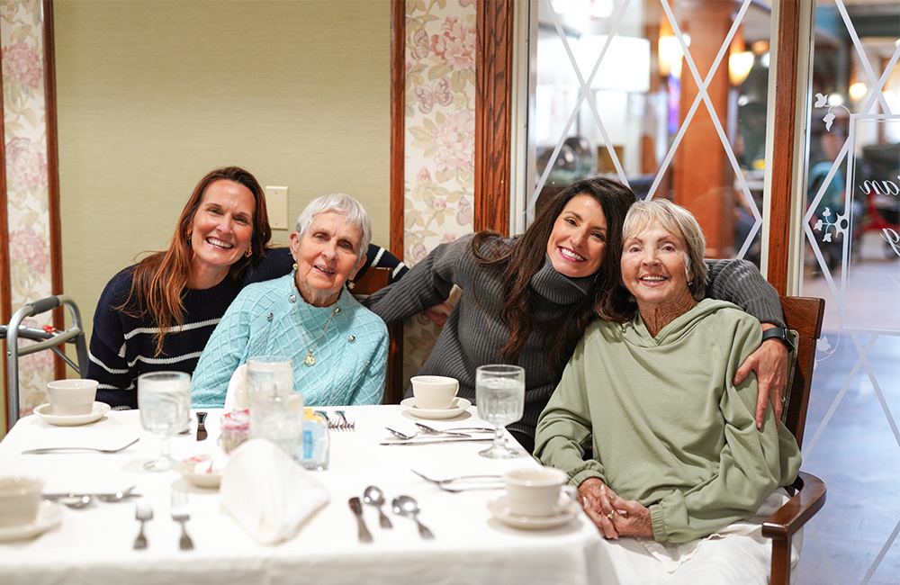 Four women sitting at a table smiling in a communal dining area.