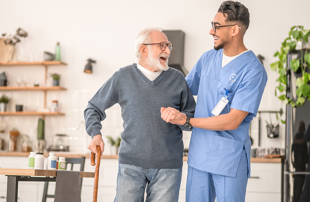 Elderly man with cane and caregiver sharing a joyful moment in a kitchen area.