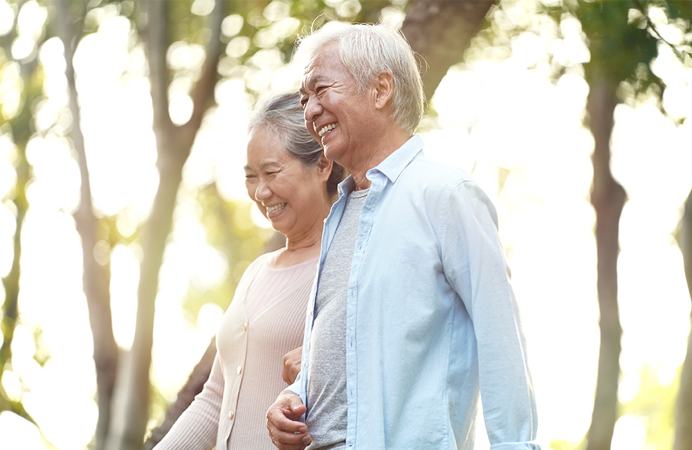 Smiling senior couple walking outdoors on a bright sunny day in a wooded area.