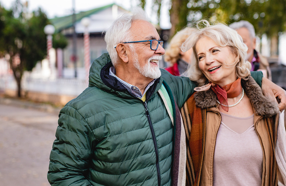 Elderly couple smiling while taking a walk outdoors in the community area.