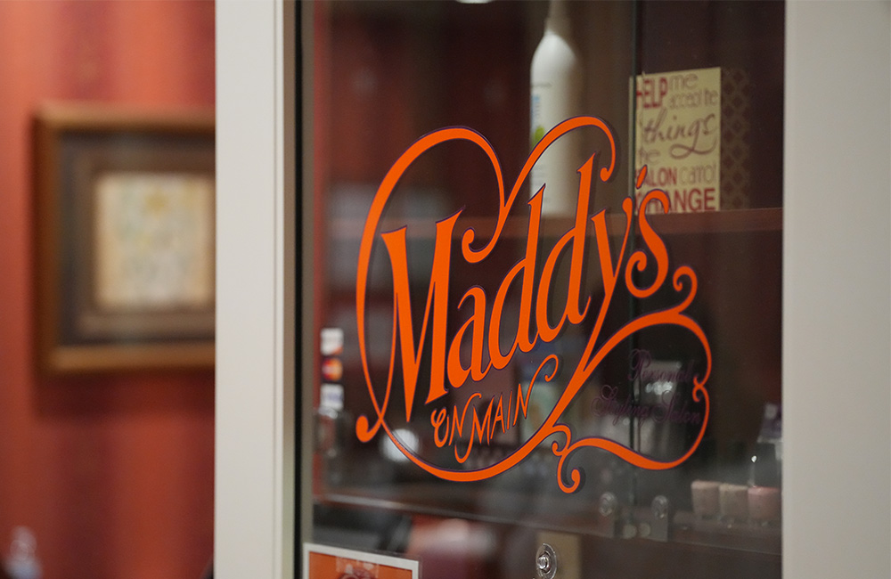 Entrance door displaying Maddys on Main in an elegant script at senior living community.