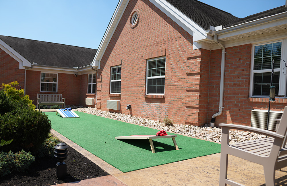 Outdoor recreation area with cornhole and seating at a senior living community.