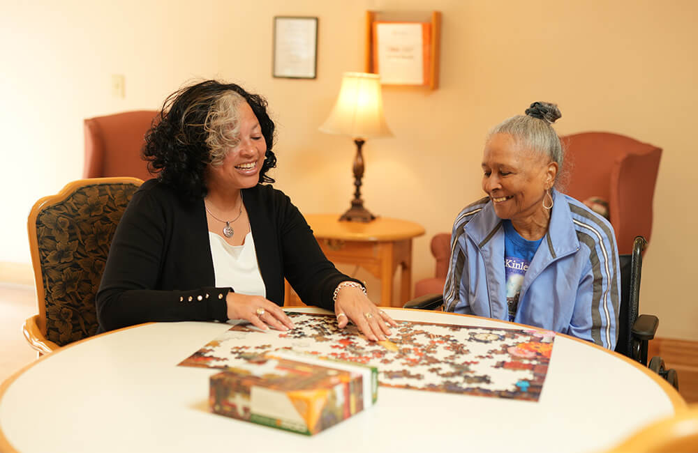 Two women enjoying a puzzle in a comfortable senior living unit.