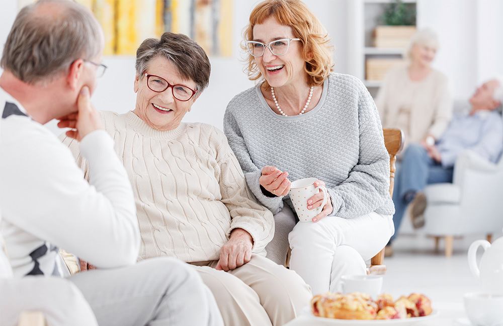 Smiling senior residents socializing in bright communal lounge area.