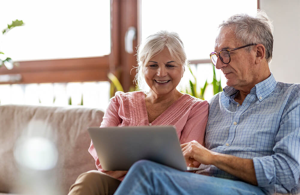 Senior couple sitting on sofa using a laptop in a well-lit living room.