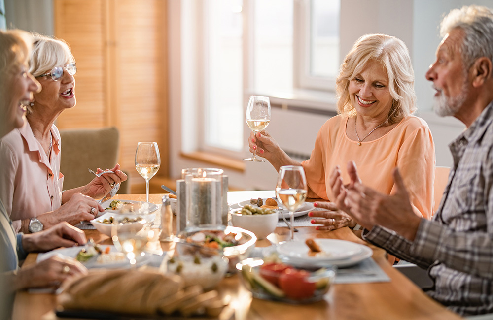 Group of seniors enjoying dinner and wine at a dining table.