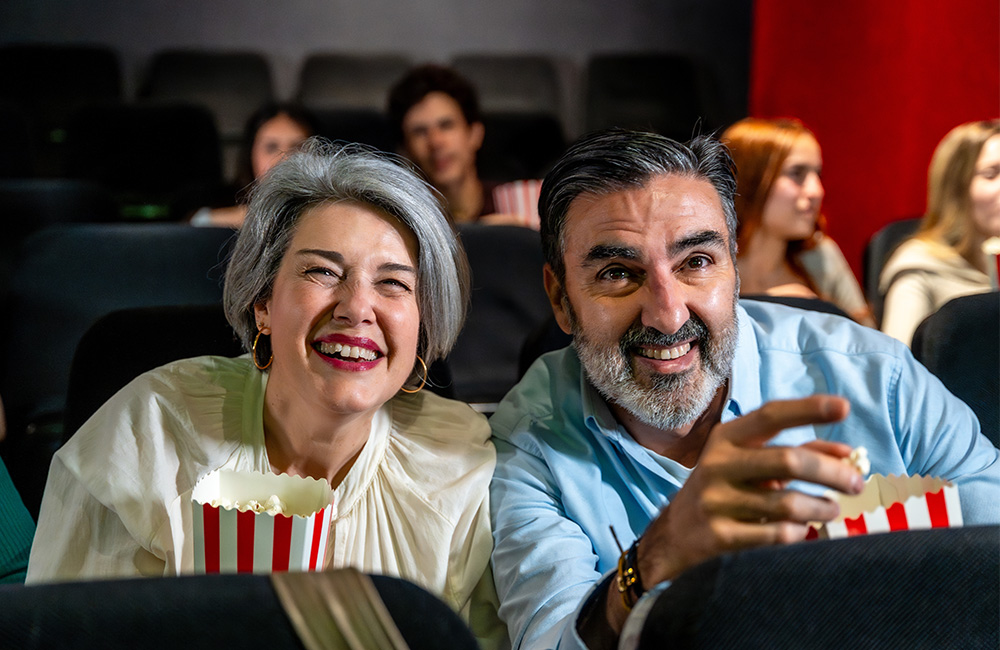 Smiling seniors enjoying popcorn at a community movie night in a theater setting.
