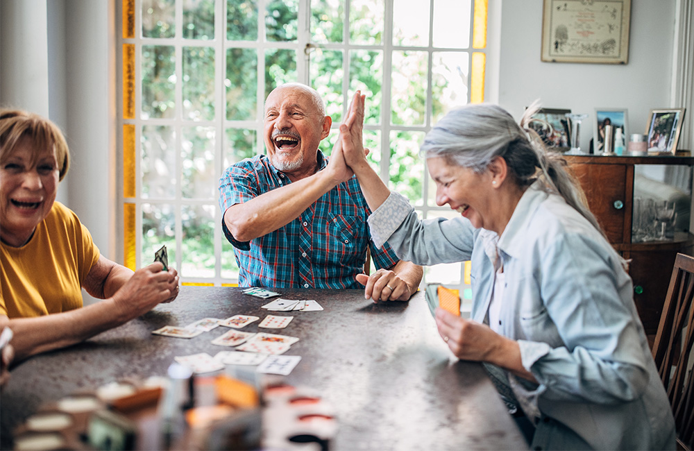 Group of seniors joyfully playing cards in a bright, sunlit room.