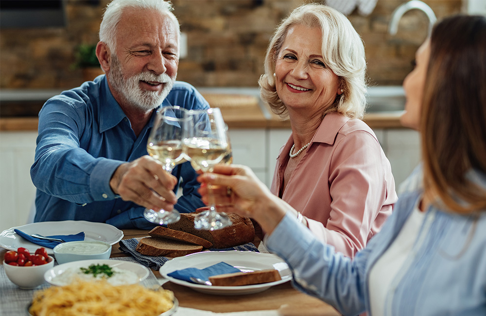 Three seniors enjoying a meal together, toasting with white wine.