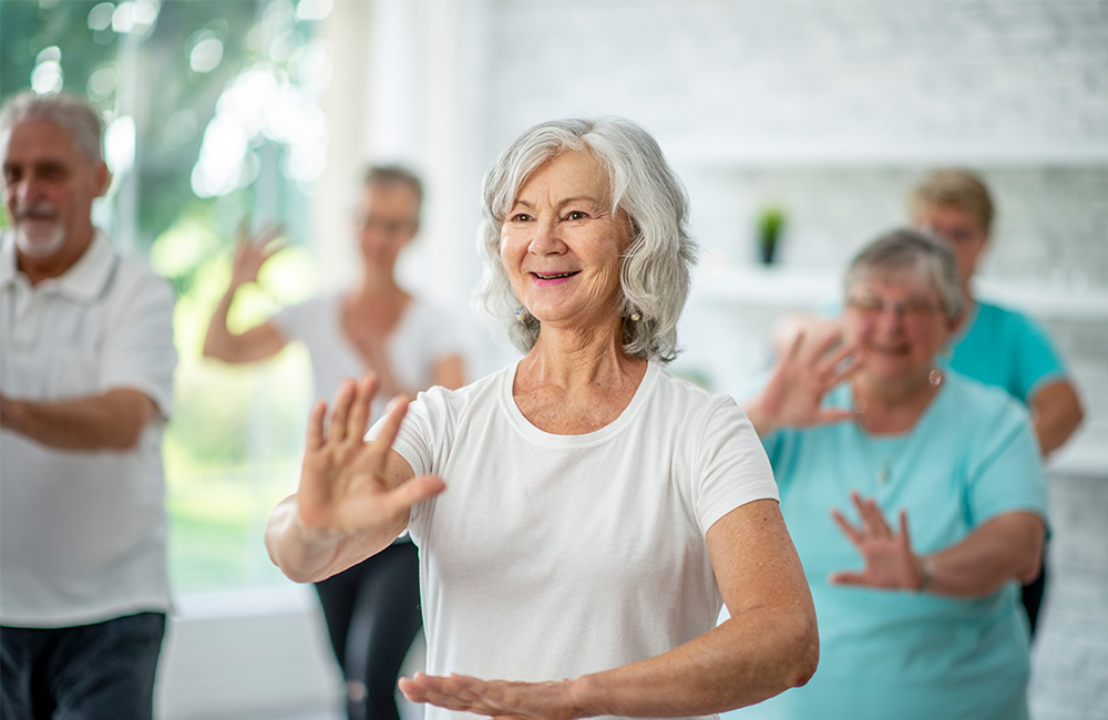 Seniors practicing tai chi in bright community room.