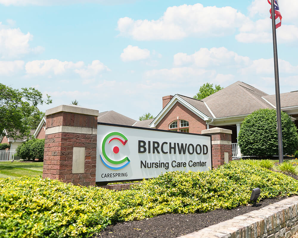 Entrance sign of Birchwood Nursing Care Center with brick building and lush greenery.