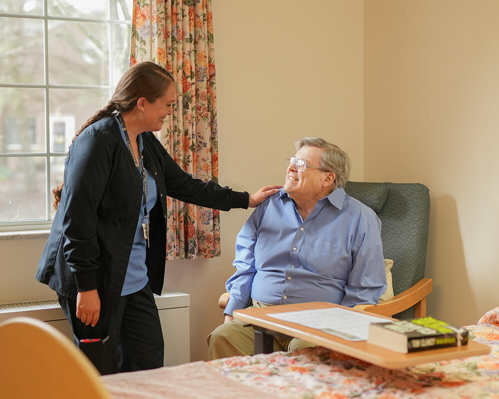 Caregiver smiling at senior resident in a cozy unit of a community setting.