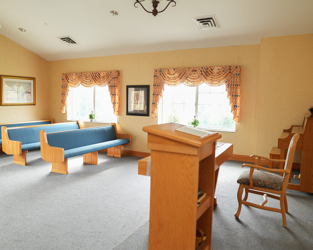 Chapel with wooden pews and podium in senior living community with large window.