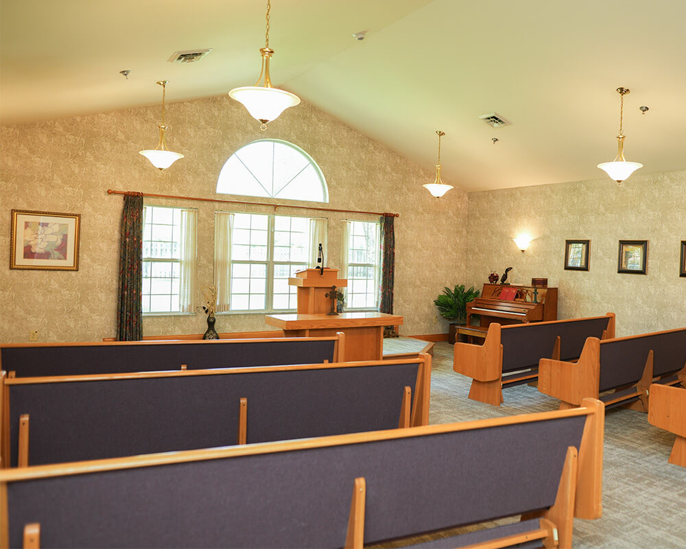 Chapel with wooden pews, a piano, and a podium in a senior living community.