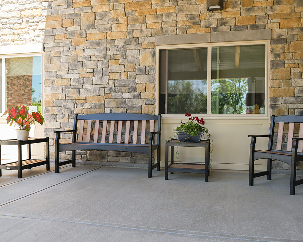 Outdoor seating with stone wall, benches, table, and potted plants at a senior community.