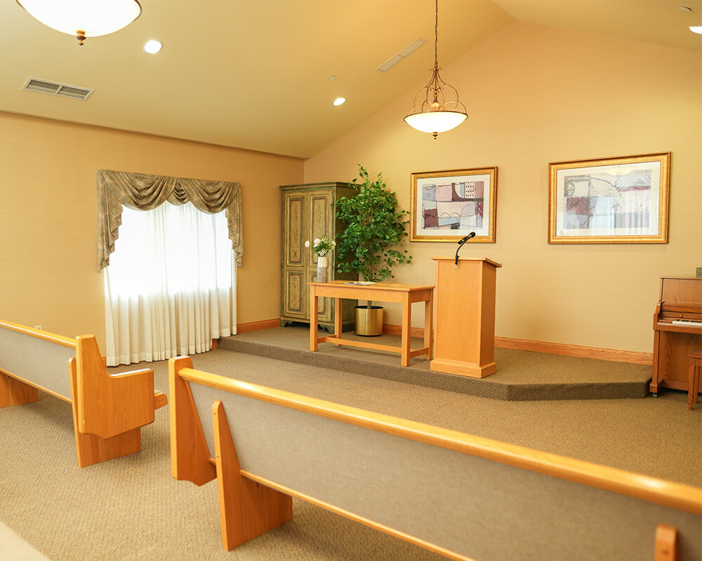 Spacious community center with seating, podium, and piano in warm lighting.