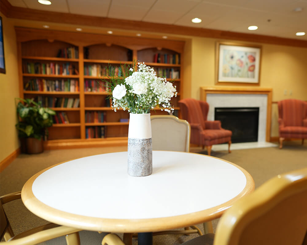 Cozy common area with table, vase of flowers, armchairs, and bookshelves.