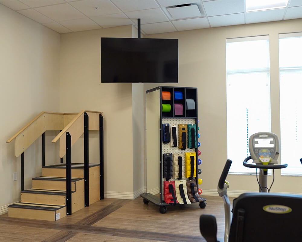 Exercise equipment and stairs in a senior living community fitness room.