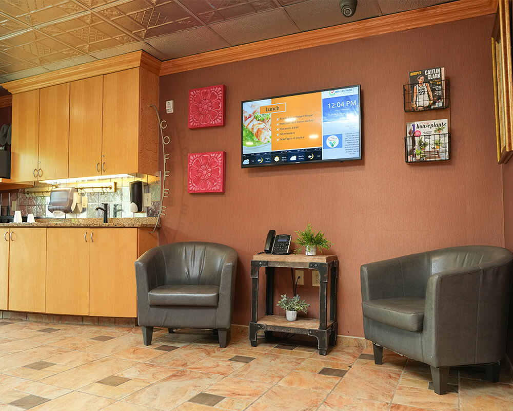 Comfortable lounge area with armchairs, a TV, and kitchenette in a community building.