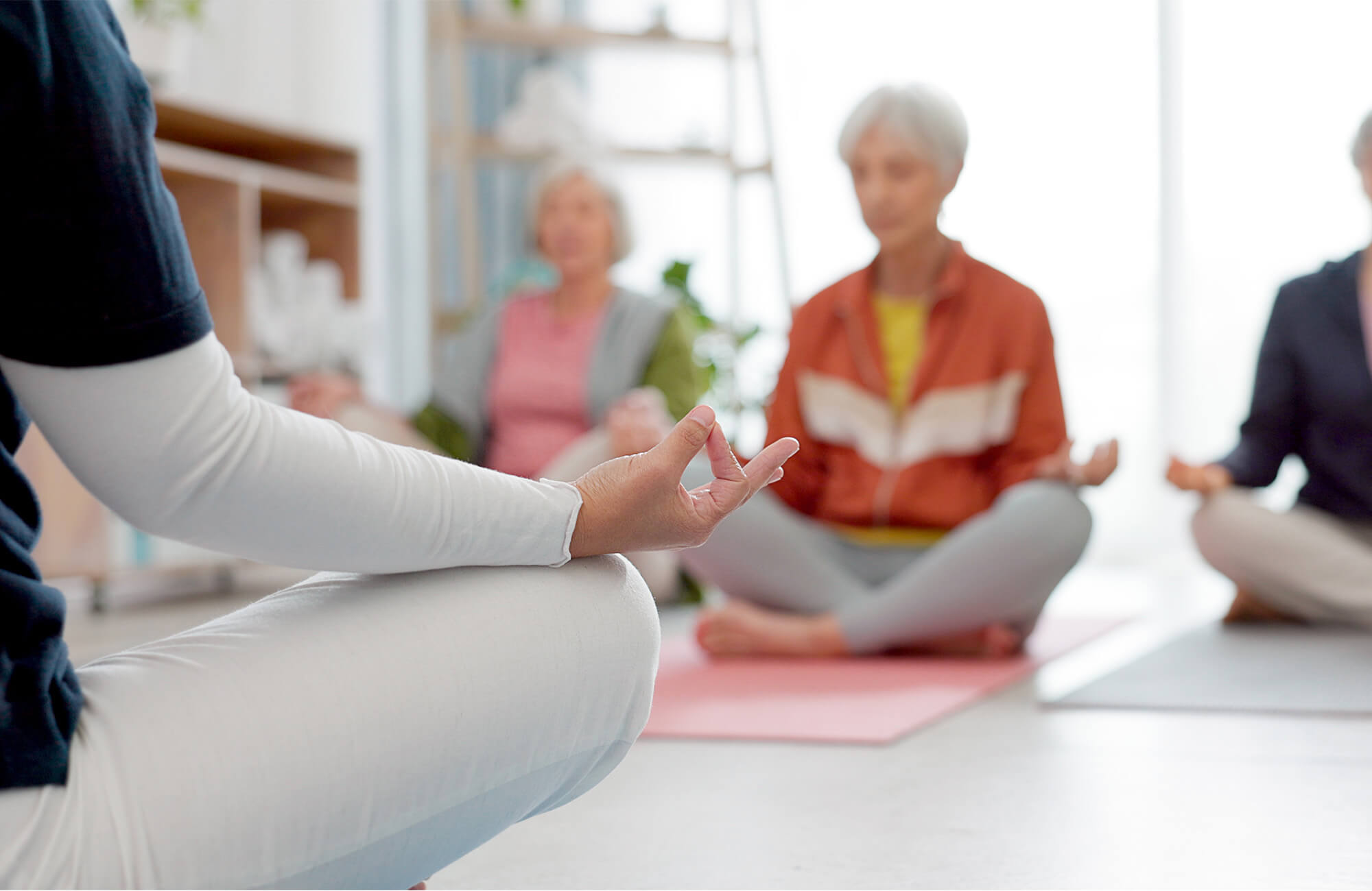 Senior yoga session with participants practicing meditation on mats indoors.