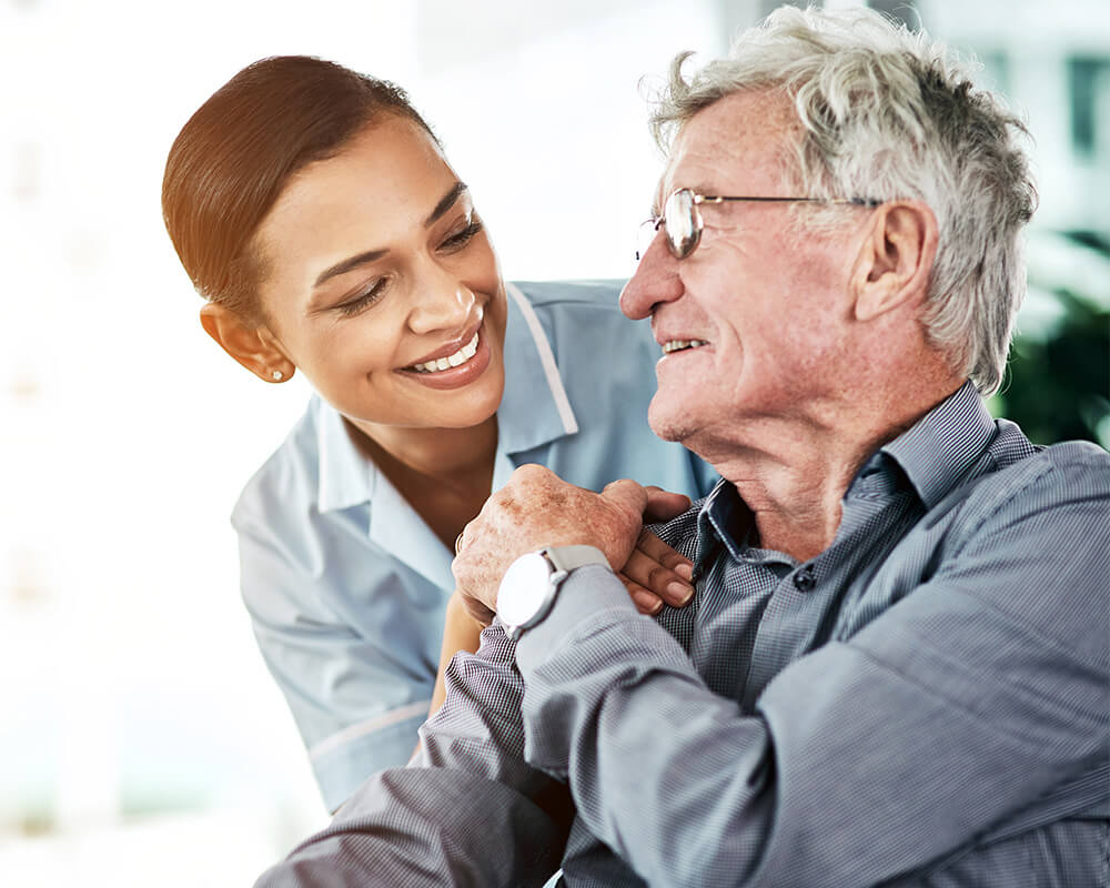 Smiling caregiver interacting with an elderly man at a senior living community.