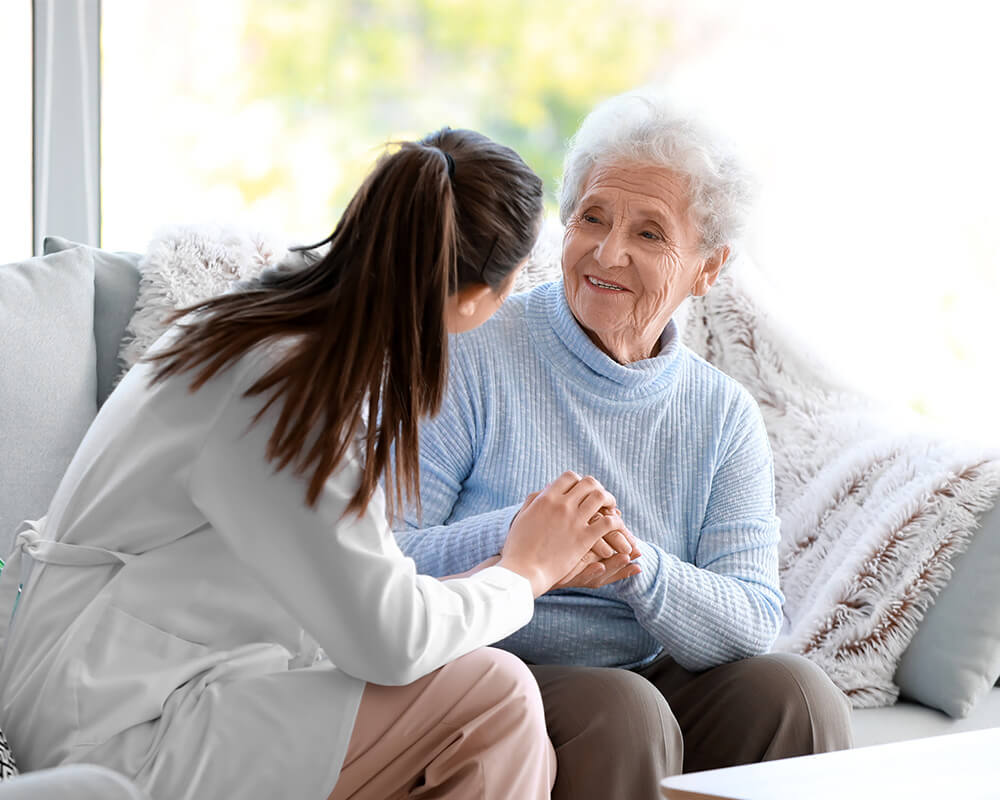 Caregiver smiling and holding hands with elderly woman in comfortable unit.