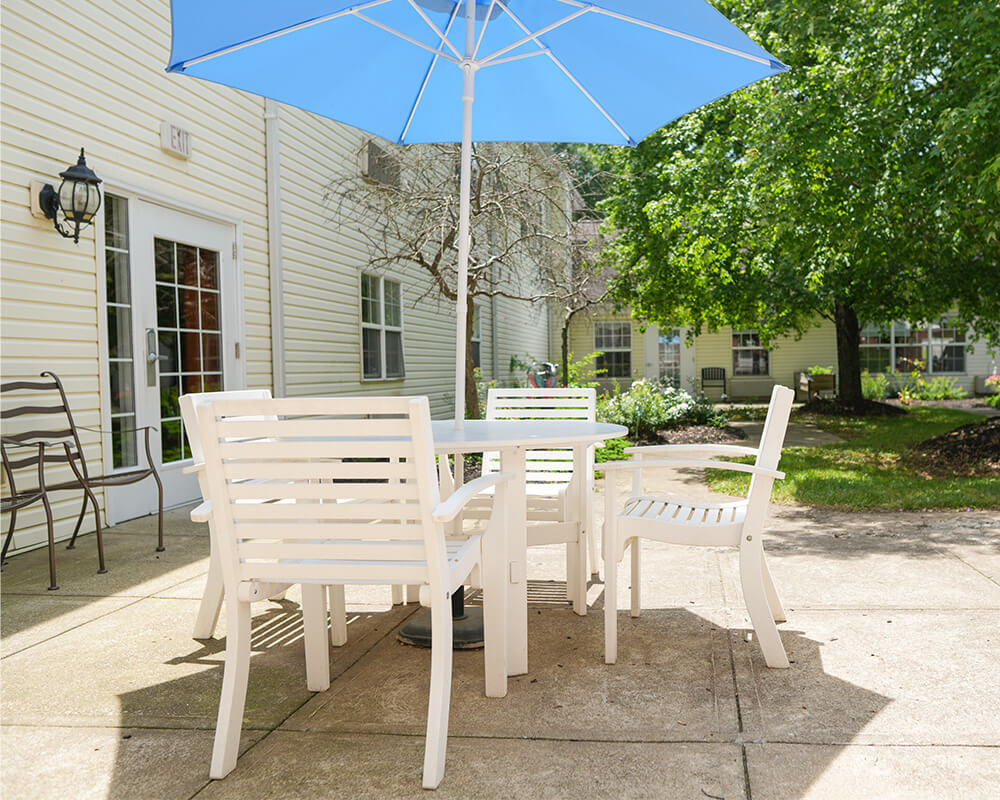 Outdoor seating area with white furniture and a blue umbrella in a garden courtyard.