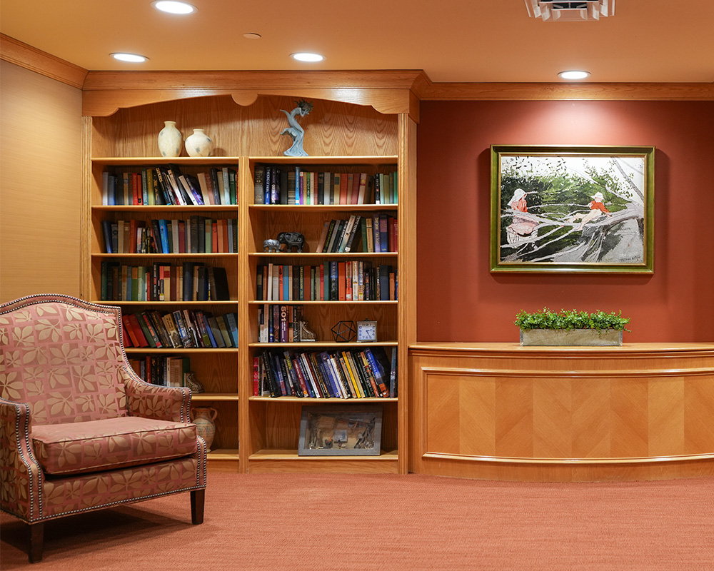 Library corner with bookshelves, an armchair, and a painting in a warm, inviting room.