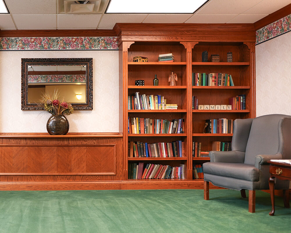Cozy reading nook with bookshelves, armchair, and decorative mirror in senior living community.