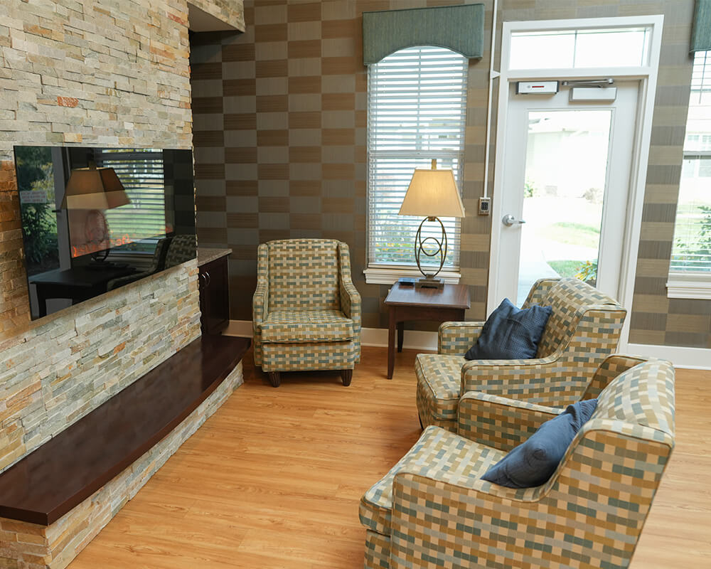 Cozy seating area with patterned chairs, a TV, and natural light in a senior living unit.